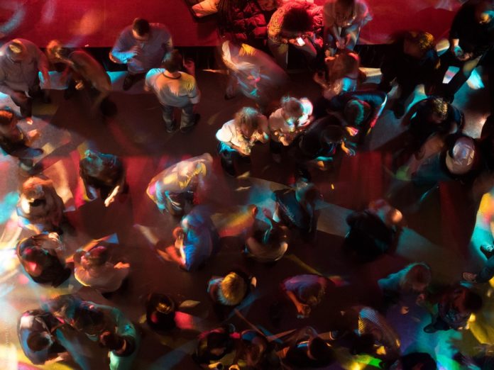 Zahlreiche Menschen tanzen und stehen in einer Bar oder in einer Disco. Es ist eine Draufsicht auf die Köpfe der Menschen.