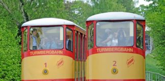 Die Turmbergbahn in Karlsruhe. Beide Bahnen fahren nebeneinander an einem hellen und freundlichen Tag. Die Fahrzeuge sind gelb und rot lackiert.