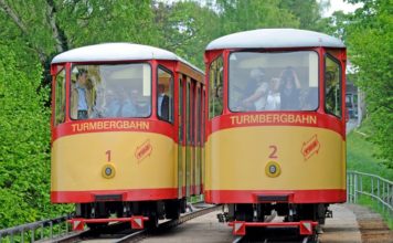 Die Turmbergbahn in Karlsruhe. Beide Bahnen fahren nebeneinander an einem hellen und freundlichen Tag. Die Fahrzeuge sind gelb und rot lackiert.