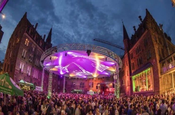 Das Hoepfner Burgfest in Karlsruhe. Eine große beleuchtete Bühne ist im Hintergrund zu sehen, davor befindet sich ein ebenso großes Publikum stehend aus tausenden Zuschauern.