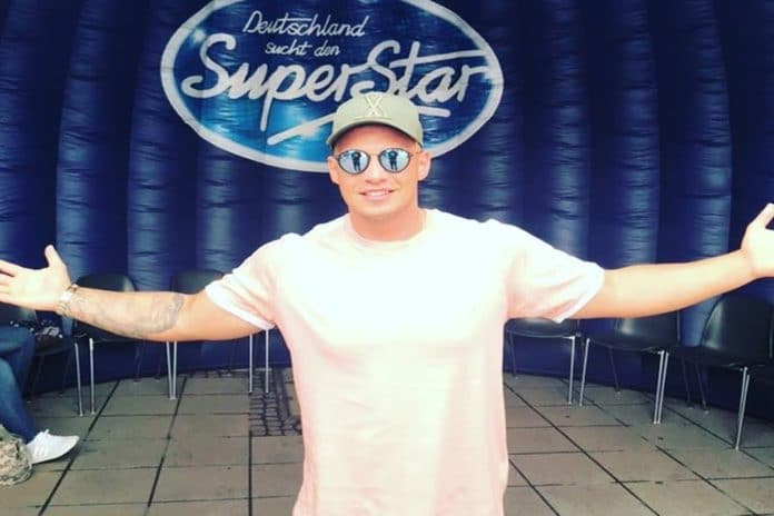 Pietro Lombardi bei DSDS auf einer kleinen Bühne vor dem berühmten blauen Logo der großen RTL-Show. Der Sänger trägt eine verspiegelte Sonnenbrille, Käppi und ein helles T-Shirt.