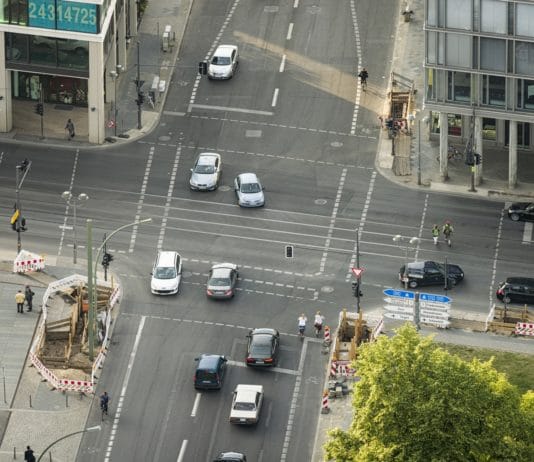 Ein Blick aus der Luft über eine große Kreuzung in einer Großstadt in der Mittagszeit, auf der viele Autos, Radfahrer und Fußgänger unterwegs sind.