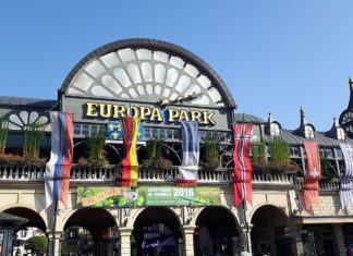 Der Haupteingang zum Freizeitpark Europa-Park mit einer überdimensional großen kuppelförmigen Uhr, verschiedenen Flaggen Europas und mehreren Steinbögen. Direkt beim Eingang befinden sich die Kassen.