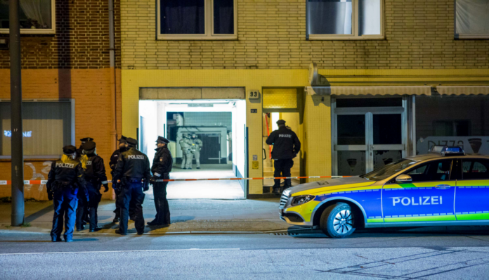 Mehrere Beamte stürmen mit einem Großaufgebot der Polizei ein Haus, um in die Wohnung zu gelangen. Sie sind bewaffnet und wollen mehrere Personen festnehmen.