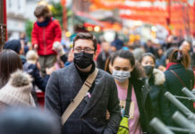 Auf dem Bild zu sehen sind jede Menge Menschen, die sich offenbar auf einer Einkaufsmeile aufhalten. Dazu tragen sie Masken, um sich vor der Ansteckung mit einem Virus zu schützen.
