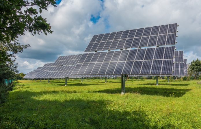 Auf einer grünen weiten Wiese stehen einige Solaranlagen, die auf Vorrichtungen installiert sind. Am strahlend blauen Himmel befinden sich zwar einige Wolken, aber die Sonne scheint, sodass die Photovoltaik-Anlage viel Energie einspeichern kann.