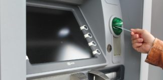 Ein Mann steckt seine Geldkarte in einem Automaten, um Geld abzuholen. Man sieht den Bildschirm mit den Tasten und das abgeschirmte Zahlenfeld zur Eingabe der PIN.