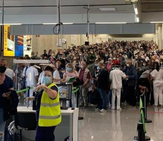 Es gibt einen großen Ansturm: Menschenmassen stehen in einem Flughafen an. Ordner in Sicherheitswesten versuchen die vielen Fluggäste zurück zu halten. Es droht ein Chaos.