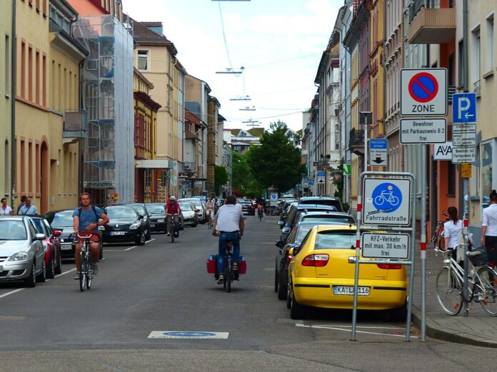 Mehrere Fahrradfahrer fahren mitten auf der Sophienstraße in Karlsruhe. Zu beiden Seiten sind eine Menge Autos geparkt. Ein Schild an der Seite sowie eines, das auf die Straße aufgemalt ist, weist darauf hin, dass es sich um eine Fahrradstraße handelt.