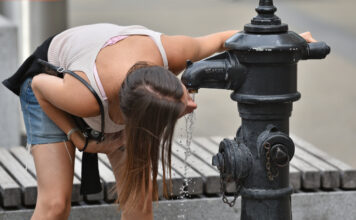 Frau trinkt bei Hitze Wasser vom Brunnen