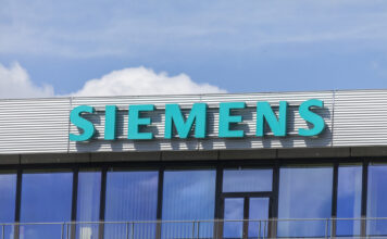 Das Siemens Geschäftsgebäude mit großem türkisem Schriftzug des Logos und des Namens. Darüber sieht man den strahlend blauer Himmel mit einigen Wolken.