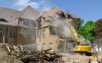 Ein Bagger reißt ein Haus ein. Das Gebäude wird abgerissen und liegt in Trümmern. Durch den Abriss entsteht eine Baustelle.