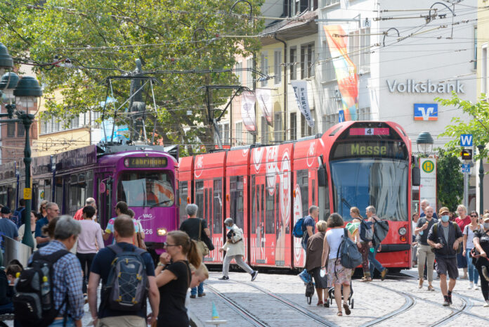 Straßenbahnen mit Menschen in einer deutschen Stadt. Die Menschen laufen zu den Zügen. Die Fahrgäste steigen ein und aus. Zum Teil bilden sich Schlangen. Mit einem bestimmten Ausweis kann man kostenlos Bahn fahren.
