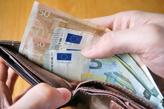 Man sieht einen Geldbeutel mit vielen Scheinen darin. Eine Hand nimmt mehrere 50- und 5-Euro-Scheine heraus oder schaut sich an, wie viel noch im Inneren ist.