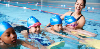 Eine Trainerin bringt Kindern das Schwimmen im Hallenbad bei.