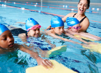 Eine Trainerin bringt Kindern das Schwimmen im Hallenbad bei.