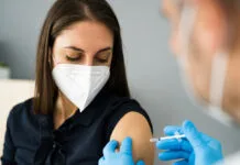 Eine Frau wird gegen Covid 19 geimpft. Sowohl die Patientin als auch die Ärztin tragen einen Mundschutz als Schutz, um eine Ansteckung und Verbreitung zu verhindern.
