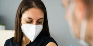 Eine Frau wird gegen Covid 19 geimpft. Sowohl die Patientin als auch die Ärztin tragen einen Mundschutz als Schutz, um eine Ansteckung und Verbreitung zu verhindern.