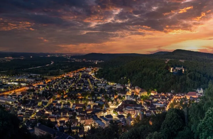 Über einer Stadt geht gerade die Sonne am Horizont unter. Die Lichter leuchten in der Stadt, die aus der Luft zu sehen ist. Es ist eine idyllische Szenerie.