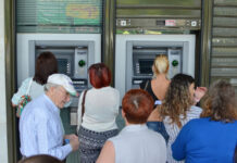 Zahlreiche Kunden stehen vor den beiden Geldautomaten einer Bank außerhalb des Gebäudes, um mit ihrer EC-Karte Bargeld von ihrem Girokonto abzuheben.
