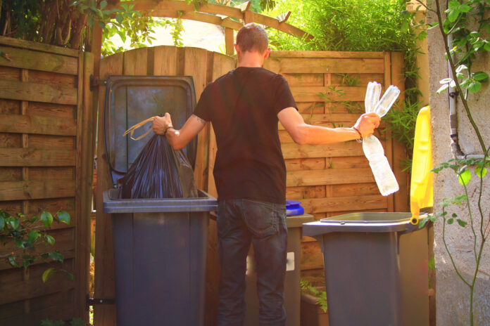 Ein Mann trennt seinen Abfall ind Restmüll und Plastik