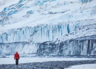 Eine Person steht vor einem schmelzenden Gletscher in der Antarktis