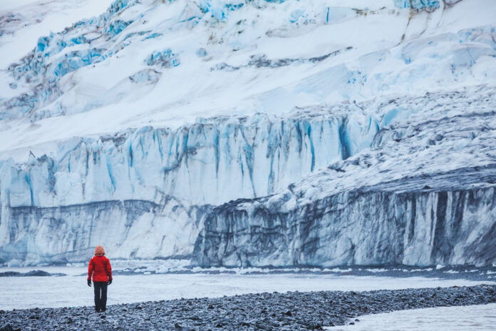 Eine Person steht vor einem schmelzenden Gletscher in der Antarktis