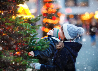Zwei Kinder stehen bei Schnee vor einem Weihnachtsbaum.