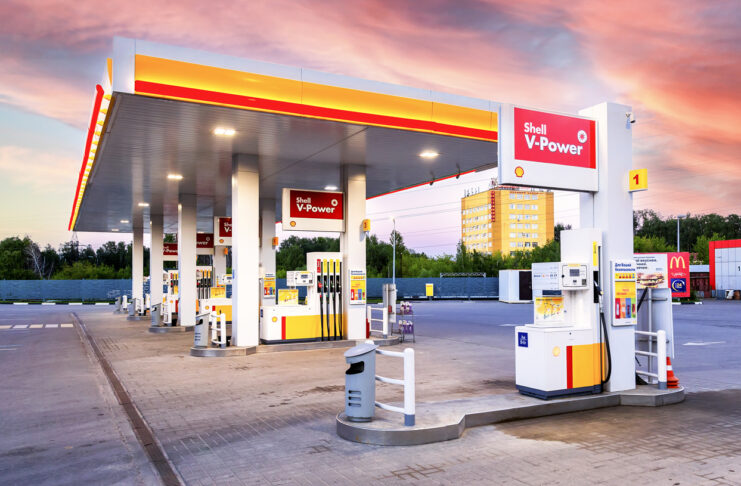 Tankstelle für Autos mit Spritpreisen. Viele Zapfsäulen bieten Benzin, Diesel und Super an. Es ist früh morgens oder spät abends. Der Himmel ist orange mit Wolken in der Dämmerung.