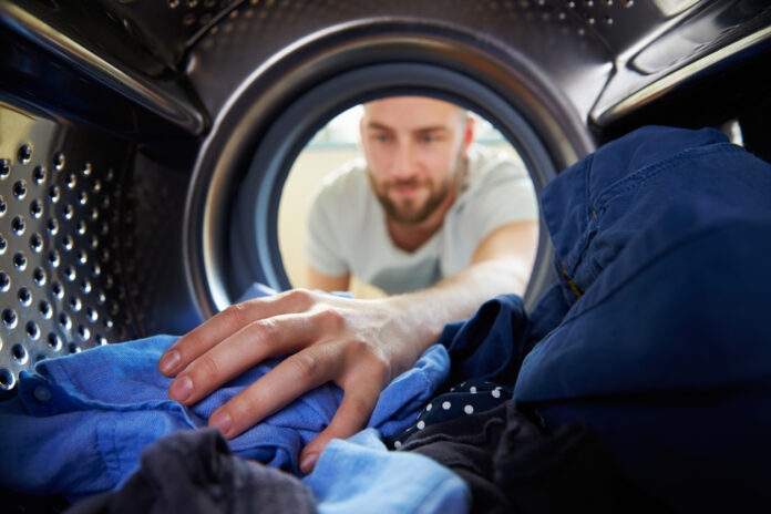 Mann legt Wäsche in die Waschmaschine.