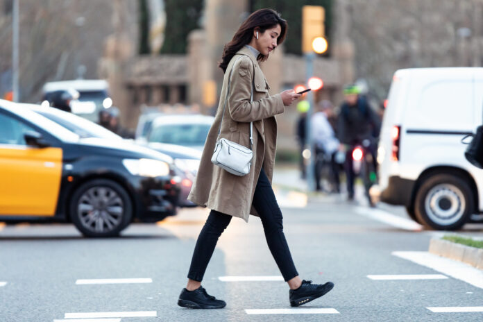 Eine Frau geht über die Straße und schaut auf ihr Handy.
