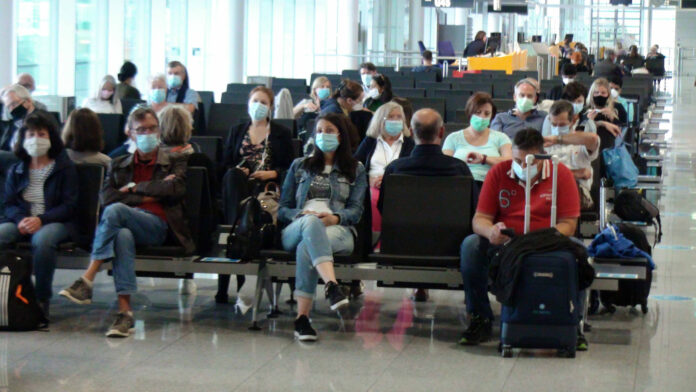 Menschen sitzen während der Corona-Pandemie mit Masken am Flughafen.