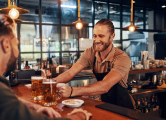 Ein lächelnder Barkeeper serviert Bier in einer Kneipe.