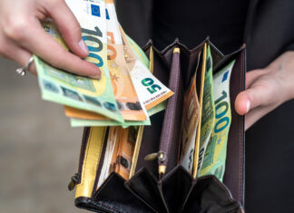Eine Frau hält ein Portemonnaie mit vielen Geldscheinen in verschiedenen Fächern in der einen Hand. In der anderen hält sie einen 100-Euro- und mehrere 10-Euro-Scheine in der Hand, die sie aus dem Geldbeutel genommen hat.