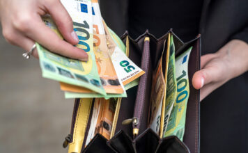 Eine Frau hält ein Portemonnaie mit vielen Geldscheinen in verschiedenen Fächern in der einen Hand. In der anderen hält sie einen 100-Euro- und mehrere 10-Euro-Scheine in der Hand, die sie aus dem Geldbeutel genommen hat.