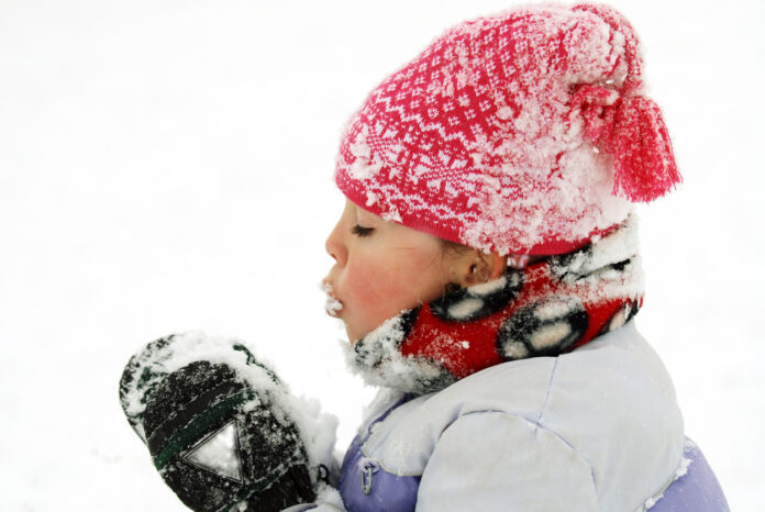 Ein Kind hat Schnee am Mund und in den Händen.