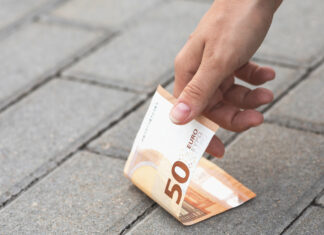 Frau findet 50 Euro auf der Straße und hebt sie auf.