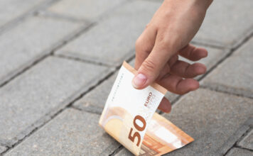 Frau findet 50 Euro auf der Straße und hebt sie auf.