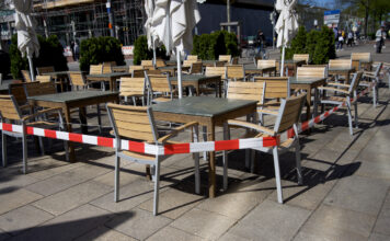 Ein geschlossener Sitzbereich eines Restaurants. Dabei hat man Tische und Stühle mit einem Baustellenband abgesperrt, sodass dort keine Gäste mehr Platz nehmen dürfen.