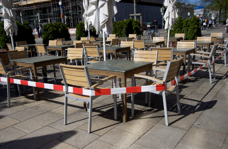 Ein geschlossener Sitzbereich eines Restaurants. Dabei hat man Tische und Stühle mit einem Baustellenband abgesperrt, sodass dort keine Gäste mehr Platz nehmen dürfen.