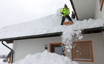 Mann schippt Schneemassen vom Dach.