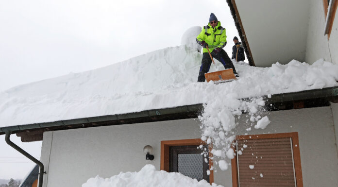 Mann schippt Schneemassen vom Dach.