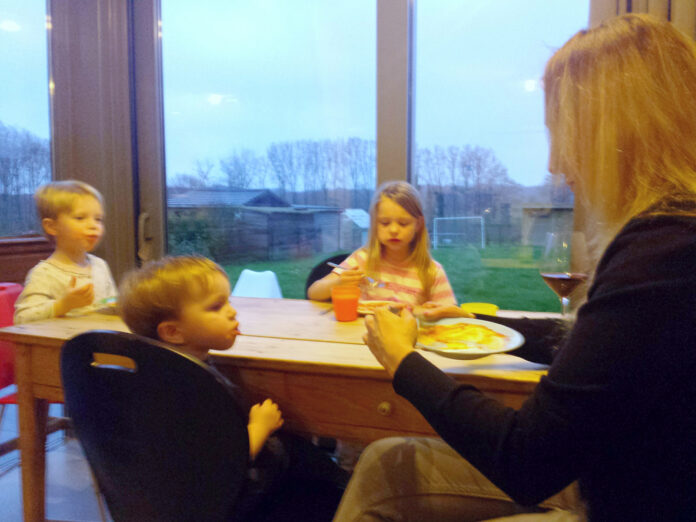 Mutter sitzt am Tisch mit ihren Kindern.