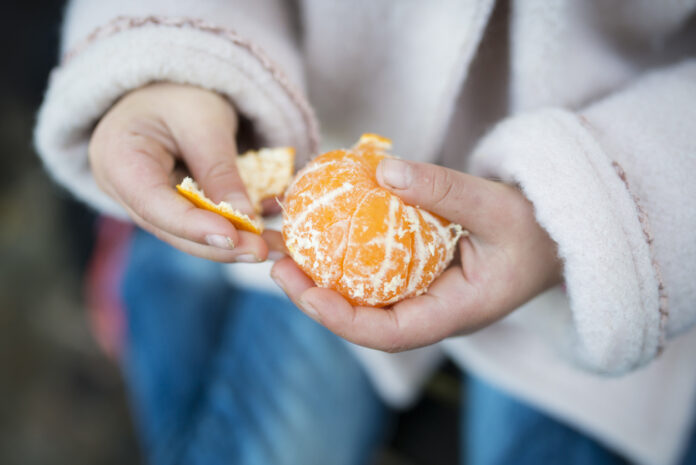 Mädchen schält eine Mandarine.