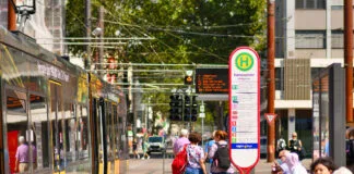 Menschen an einer Bushaltestelle in Karlsruhe. Die Fahrgäste warten auf den Bus oder die S-Bahn. Per ÖPNV wollen sie dann ans Ziel kommen.