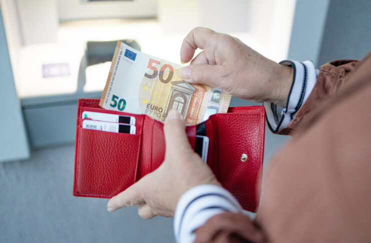 Eine Frau hält in der linken Hand ein rotes Portemonnaie und holt Geld aus ihrem Geldbeutel. Dabei handelt es sich um einen 50-Euro-Schein, den sie gerade herauszieht.