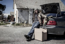 Ein obdachloser Mann steht an seinem Auto