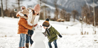 Familie baut einen Schneemann im Winter, um sie herum schneit es