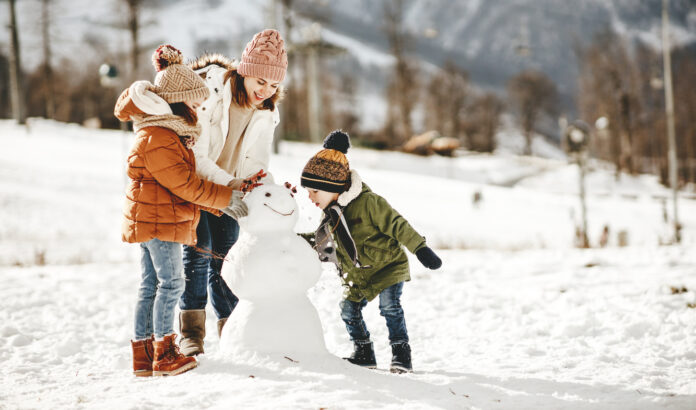 Familie baut einen Schneemann im Winter, um sie herum schneit es