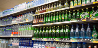 In einem üblichen Supermarkt sind in einem Regal viele Flaschen Wasser, Plastikflaschen und Glasflaschen sortiert und geordnet nebeneinander aufgereiht und ordentlich in einer Linie sortiert.